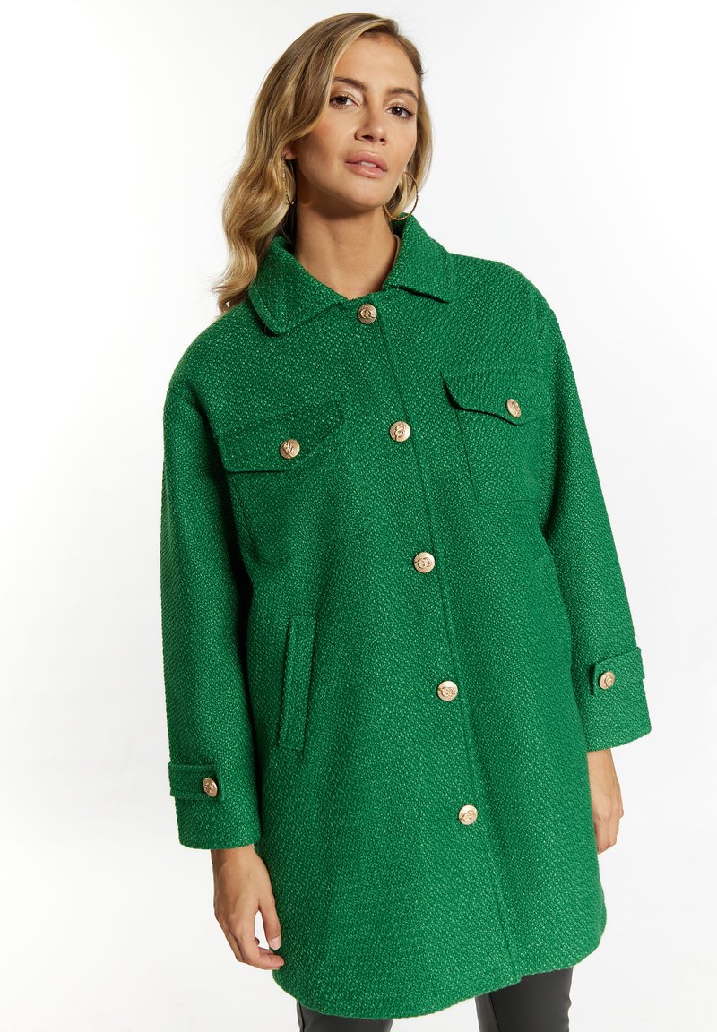 Cappotto verde testurizzato con colletto, due tasche sul petto e bottoni dorati. Maniche lunghe con polsini abbottonati.