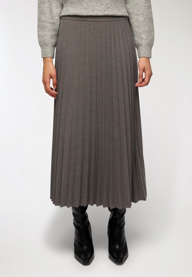 Gonna plissettata grigia realizzata in tessuto morbido, con vita elastica e silhouette fluida, abbinata a stivaletti neri alla caviglia.
