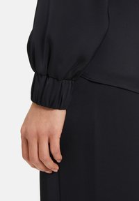 Zwarte lange mouw kledingstuk met een gesmockte manchetdetail, met een gladde, zachte textuur en een elegante silhouet.