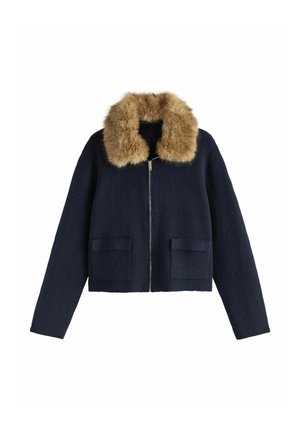 Mornarsko plava vunena skraćena jakna s ovratnikom od umjetnog krzna, prednjim zatvaračem na patentni zatvarač i dva teksturirana džepa s flasterima. Dugih rukava i kroja koji prati tijelo.