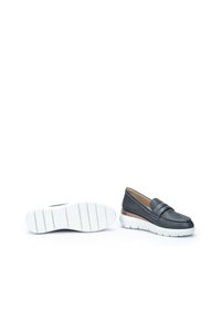 Scarpe slip-on nere perforate con un'accentuazione in pelle marrone liscia e suola in gomma bianca. Presentano una fascia larga sul davanti.