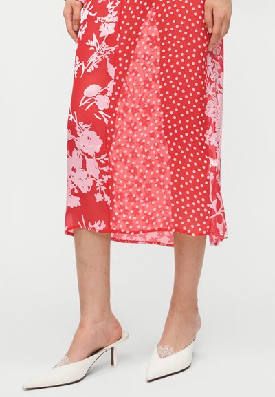 Κόκκινο φόρεμα με λουλουδένια και βουλοκέτο σχέδια, διαφανές ύφασμα. Λευκά mules με μυτερά δάχτυλα και χαμηλά τακούνια, με δαντελένιες λεπτομέρειες.