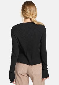 Schwarzes, geripptes Langarmoberteil mit cropped Schnitt, rohen Saumkanten und verlängerten Ärmeln. Kombiniert mit beigen Cordhosen.