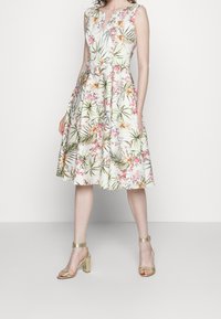 Robe à imprimé floral blanche avec un corsage ajusté et une jupe évasée. Comprend des feuilles vertes, des fleurs roses et jaunes, ainsi qu'un décolleté en forme de clé.