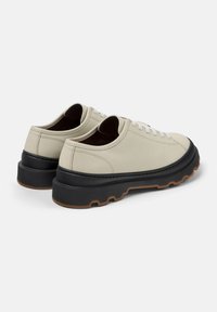 Sneaker chiari con suola nera spessa, dotati di lacci e cuciture bianchi, mostrati da una vista posteriore diagonale.