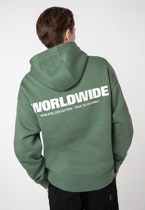 Hooded sweatshirt in dark green with large white lettering on the back reading "WORLDWIDE SUBLEVEL COLLECTION - TRUE TO YOURSELF." Soft texture.