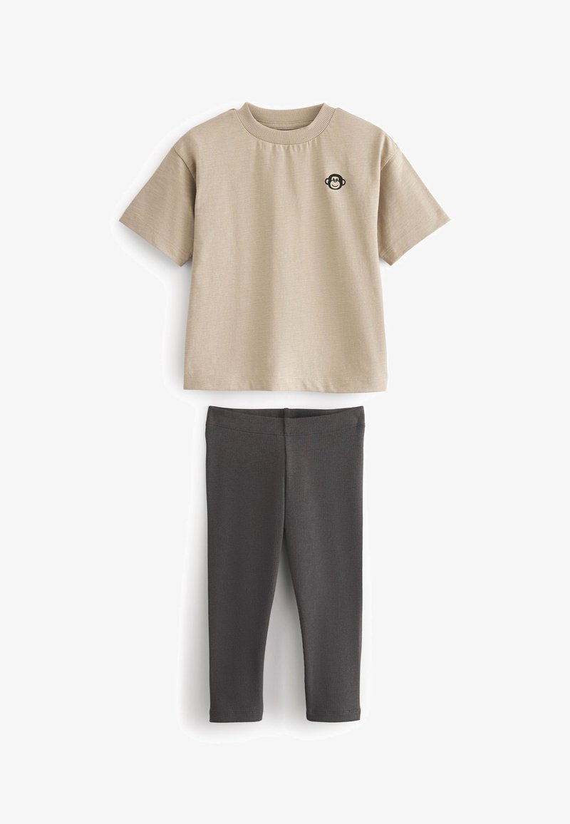 Beige Kurzarmpullover mit Rundhalsausschnitt und einem Affenlogo; kombiniert mit dunkelgrauen Leggings mit gerippter Textur.