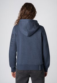 Marineblauwe hoodie met ribbelboorden aan de manchetten en onderkant. Kenmerken zijn logo tekst gedrukt op de rechtermouw en achterkant, gemaakt van zachte, gestructureerde stof.
