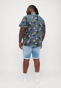 Camisa de manga corta con estampado floral en tonos azules y verdes, combinada con pantalones cortos de mezclilla azul claro y zapatillas blancas. Estilo casual, ajuste relajado.
