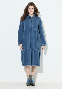 Pitkä farkkukleid, jossa on napitettava etuosa, kärkitasku ja kerrostettu hame. Varustettu pitkillä hihoilla ja kerroksellisella suunnittelulla, jossa on kontrastiväriset ompeleet.