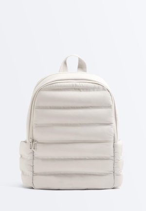 Svetlo bež nahrbtnik z vodoravnim prešitim vzorcem, žepom z zadrgo spredaj, dvojno zadrgo, stranskimi žepi in zgornjim ročajem za nošenje.