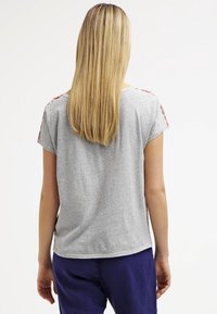 Grijze t-shirt met korte mouwen en een comfortabele pasvorm. Heeft bloemenpatronen op de schouders. Gemaakt van zachte, lichte stof.