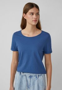 T-shirt bleu à manches courtes avec un col rond et des manches roulées, fabriqué en tissu doux avec une texture lisse.