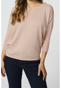 Ljusrosa stickad tröja med avslappnad passform, trekvartsärmar och ribbade detaljer, i kombination med mörkblå jeans. Mjuk textur.