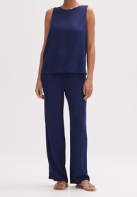 Granatowy bezrękawnik połączony z dopasowanymi spodniami typu "wide-leg", wykonanymi z gładkiego materiału. Sandały na cienkich paskach dopełniają całość.