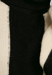 Pull en maille épaisse avec des rayures verticales noires et crème, col montant et texture côtelée sur chaque section de couleur.