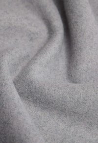 Tela gris claro con una superficie suave y texturada, que exhibe tonos sutiles y un acabado liso y no reflectante, arreglada en pliegues.