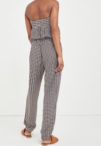 Trykt jumpsuit med smocket bodice, bred ben og et geometrisk mønster i hvid, marineblå og bordeaux; letvægtsstof; set fra ryggen.