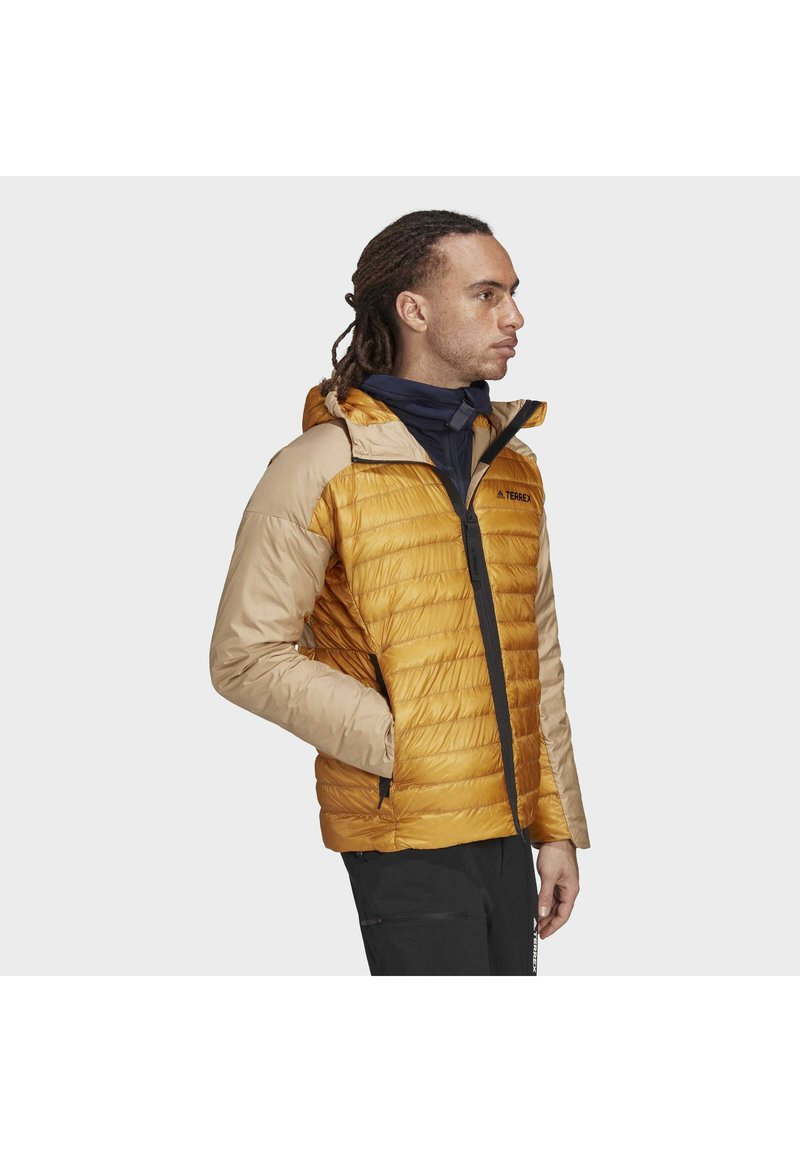 Gefütterte Jacke mit gelbem Körper und beigen Ärmeln, ausgestattet mit einer Kapuze, einem Reißverschluss vorne und seitlichen Taschen. Strukturierter Stoff mit Nähdetails.