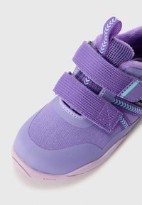 Violets sporta apavi ar diviem Velcro siksnām, teksturētu auduma augšdaļu un gumijas zoli. Iezīmējas ar gaiši violetiem akcentiem un zigzaga rakstu.
