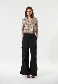 Seidige Bluse mit Muster in warmen Tönen und Kragen, kombiniert mit hoch geschnittenen schwarzen Cargo-Hosen mit mehreren Taschen und weitem Bein.