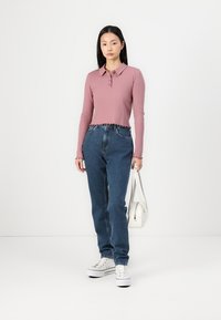 Ribbet rosa langermet polo-skjorte med knappestolpe, kombinert med høytsittende blå jeans. Modell bærer en hvit håndveske og har på seg hvite sneakers.