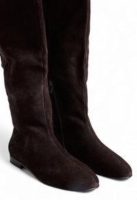 Las botas negras de ante hasta la rodilla tienen un dedo del pie puntiagudo, una suela plana y un zipper lateral para fácil uso. La textura parece suave y delicada.