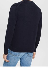 Mörkblå stickad tröja med rundad hals och ribbade ärmmuddar, med en texturerad finish och avslappnad passform, tillsammans med ljusblå jeans.