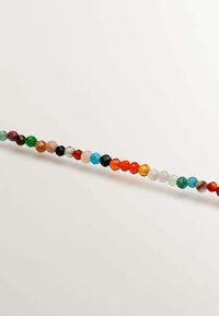 Perlas decorativas multicolores de diversos tamaños, con formas redondas y facetadas, dispuestas en un patrón lineal sobre un fondo claro.
