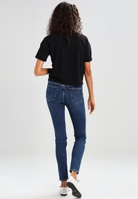 Svart kortärmad t-shirt i kombination med blå slim-fit jeans som har bakfickor och en mjuk denimtextur. Modellen bär vita skor.