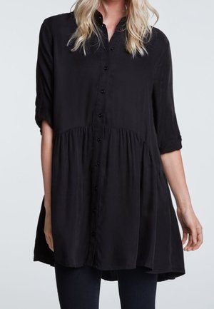 Musta pusero, jossa on napitettu etuosa, mandariinikaulus ja kolme neljäsosaa hihan pituudesta. Siinä on kerrostettu, levenevä malli ja kevyt kangas.