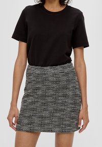 Žena v černém tričku s krátkým rukávem, zastrčeném v sukni s vysokým pasem, která je texturovaná a má černo-bílé pruhy.
