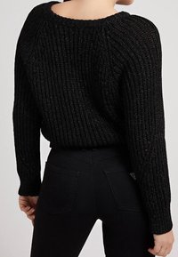 Pull noir en maille avec une texture côtelée, un large col et une coupe décontractée. Associé à un jean noir taille haute avec des poches arrière.