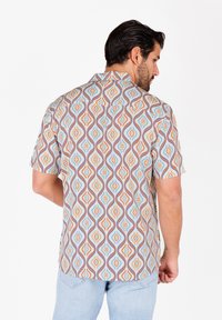 Camisa de manga corta en tejido ligero con un patrón de remolinos geométricos en múltiples colores. Los colores incluyen azul, naranja y beige. Presenta un cuello estándar.