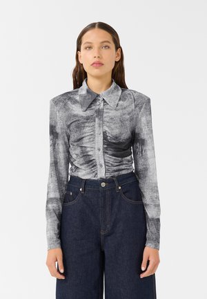 Long-sleeve shirt in black and gray with a textured pattern and button-up front, paired with high-waisted dark denim pants.