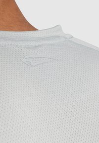 Jasnoszara koszulka sportowa z oddychającą siateczką, z subtelnym logo nadrukowanym w okolicy dekoltu dla dodatkowego akcentu.