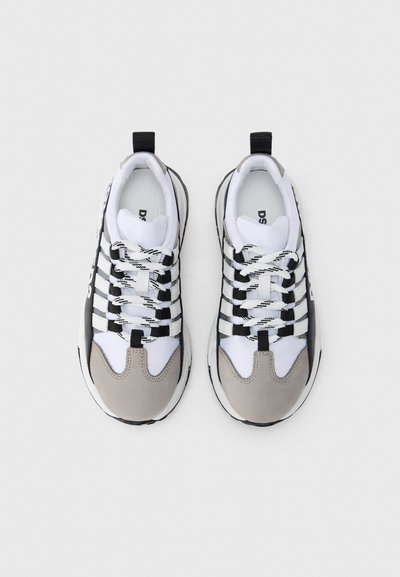 Chaussures de sport blanches et grises avec une tige en mesh, des accents en daim, des sangles noires, des lacets à motifs, une semelle en caoutchouc et une languette au talon.