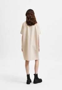 Beige, nadměrné šaty košilového střihu z hladkého materiálu s krátkými rukávy a zaobleným lemem, doplněné černými kotníkovými botami.
