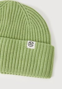 Grønn strikket lue med ribbet tekstur, med en brettet mansjett og en liten hvit etikett med logo.
