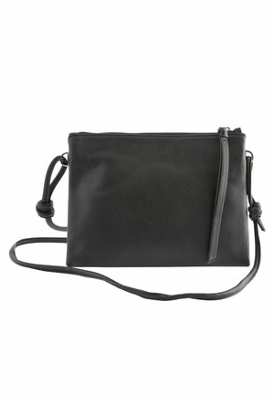 Sac bandoulière en cuir noir avec bandoulière réglable, fermeture éclair supérieure et un détail de nœud noué aux deux extrémités de la bandoulière.