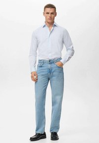 Jeans de mezclilla azul claro con corte recto, combinados con una camisa blanca de botones con rayas azul claro. Zapatos negros como calzado.