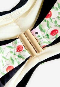 Bikini top featuring a cream base, black accents, and a floral print band with red and pink accents, secured by a gold-tone clasp.