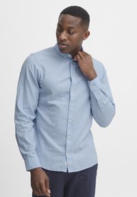 Light blue, button-up shirt in a plain weave fabric with a pointed collar and long sleeves. Features small round buttons and a curved hem.