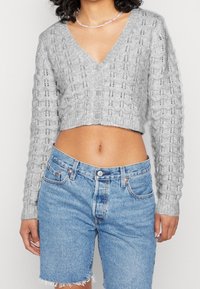 Szary krótki kardigan z dekoltem w kształcie litery V, teksturowanym wzorem dzianiny i przednimi guzikami, zestawiony z jasnoniebieskimi szortami z wysokim stanem wykonanymi z denimu.