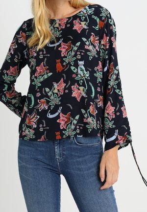 Haut à manches longues, navy avec imprimé floral et animal en rose, vert et rouge. Présente un détail froncé sur le côté, un tissu léger et une coupe décontractée.
