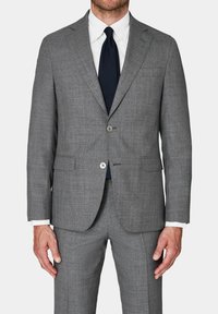 Giacca da abito grigia con una finitura testurizzata, chiusura con un unico bottone, due tasche con patta, indossata sopra una camicia bianca e una cravatta blu navy.