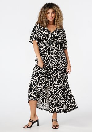 Zwart en beige maxi-jurk met bloemmotief, met een vooraan geknoopte sluiting, korte mouwen en een vloeiende silhouet; gecombineerd met zwarte, gespsandalen.