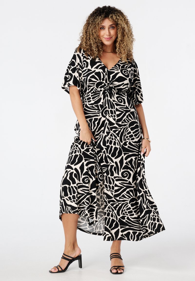 Zwart en beige maxi-jurk met bloemmotief, met een vooraan geknoopte sluiting, korte mouwen en een vloeiende silhouet; gecombineerd met zwarte, gespsandalen.