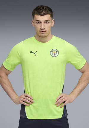 Leuchtend grünes Sport T-Shirt mit kurzen Ärmeln, Puma-Logo auf der linken Brust, Manchester City Abzeichen, strukturierter Stoff und marineblaue Akzente an den Seiten.