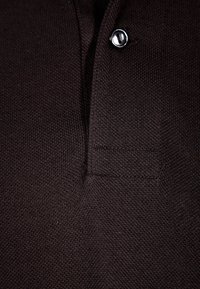Gros plan d’un tissu noir texturé avec un bouton et un détail de poche sur un vêtement de style polo.